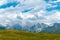 People, hikers walk far in the long distance, on a summer sunny day, against the background of snow-capped peaks of the Caucasus