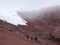 People hiking at a vulcano, through the red sand towards the first snow of the gletser
