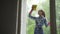 People, housework and housekeeping concept - happy woman in gloves cleaning window with rag and cleanser spray at home