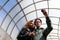 People inside the pedestrian crossing with a glass dome and old gray walls. A young African-American girl and a European guy in ja