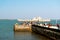 People, men, women, children walking on a jetty at Diu fort with Pani Kotha prison in the distance