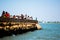 People, men, women, children walking on a jetty at Diu fort with Pani Kotha prison in the distance