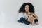 People, pet care and friendship concept. Smiling Afro woman with glad expression cuddles pedigree dog, sit on comfortable bed,