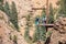 People on a platform in the mountains getting ready to rappel down - man helping woman in harness as she gets ready to go while