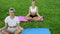 People practicing yoga on grass in the park. Girls meditating, sitting in lotus pose outdoors at sunset