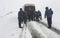 People pushing stuck car in snowy mountain