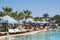 People relax by the pool with sun loungers, parasols and palm tr