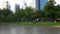 People relax in public park with lake and green trees with skyscrapers buildings