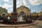 People rest at the fountain in the station square in front of the main railway station of the city on a sunny summer day