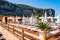 People resting on deckchairs under white parasols on wooden terrace in Vico Equensea coastal town near Naples with rocky mountains