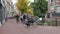 People riding bicycles through a paved urban city center location with bikes parked in