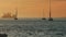 People sailing on a sailing boat during orange sunset - industrial cranes on the background