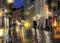 People silhouette with umbrella walk on evening street blurred city light reflection lantern and shop vitrines in Tallinn old town