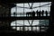 People silhouetted on a walkway in a building near the windows