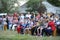 People sitting on benches on a rural lawn during concert devoted to the Day of village