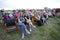 People sitting on benches on a rural lawn during concert devoted to the Day of village