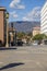 People sitting in a courtyard surrounded by apartments,shops and tall brown light posts with mountains, clouds