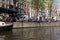 People sitting at sidewalk cafe by canal with facades of traditional houses in background. Amsterdam