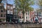 People sitting at sidewalk cafe by canal with facades of traditional houses in background. Amsterdam