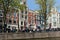 People sitting at sidewalk cafe by canal with facades of traditional houses in background. Amsterdam, Netherlands
