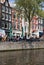 People sitting at sidewalk cafe by canal with facades of traditional houses in background. Amsterdam, Netherlands