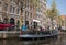 People sitting at sidewalk cafe by canal with facades of traditional houses in background. Amsterdam, Netherlands