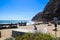 People sitting on a wooden benches overlooking the vast blue ocean water surrounded by lush green plants and rocks