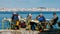 People sitting at yellow restaurant tables in the shore of the river Tagus in Cacilhas - Lisbon`s cityscape in the
