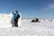 People on a snowmobile passing through a frozen river past a man building a snow wall