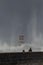 People standing on a pier observing the turbulent waves crashing against a lighthouse on a misty day