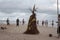 People and the Straw Scarecrow stand on a sandy beach on the ocean shore during a ceremony for good weather and good fishing