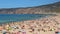 People sunbathing on crowded beach, waves rolling onto seashore, sunny summer