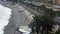 People sunbathing on pebble beach by ocean, active traffic on road, resort city