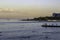 People swim in the sea and relax on the shore against the backdrop of a height of houses illuminated by the sun at sunset.