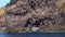 People swimming near boat in Mediterranean sea, behind rock with hole, Lipari Island. Summer sunny day, blue sky. Sicily