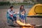 People, tourism and nature concept - Romantic evening, man embrace woman sitting near a campfire