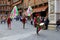 People in traditional costumes with flags and drums are going on Piazza del Campo past tourists in Contrada Day.