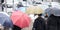 People under umbrellas waiting at pedestrian street crossing in a busy street on a rainy day in the city