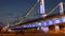 People walk along comfortable embankment at bridge with bright colored lights