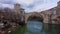 People walk on ancient arched stone bridge over river