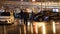 People walk through the night city after rain between parked cars.