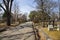 people walking along a footpath in the graveyard with headstones, graves, bare trees, lush green trees, plants