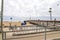 People walking along the pier at the beach with blue tents in the sand, bike racks and bikes on a cloudy day