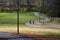 People walking along winding footpaths in the park surrounded by lush green grass, tall black lamp posts, lush green trees