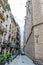 People walking down an alley/narrow street in an area of both residential and commercial properties in Barcelona.