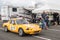 People walking down a paddock looking at a racing car  driving past.  Motion blur