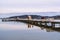 People walking on a long pier reflected in the water, on a calm winter day.