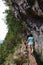 People walking on a narrow path on the edge of the rock during Levada do Caldeirao Verde Trail. Rocks and green trees. Dangerous