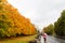 People walking on the sidewalk with umbrellas, against the background of the Avenue of autumn Park. Autumn season. Copy space