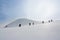 People walking with snow rackets towards the summit of a hill